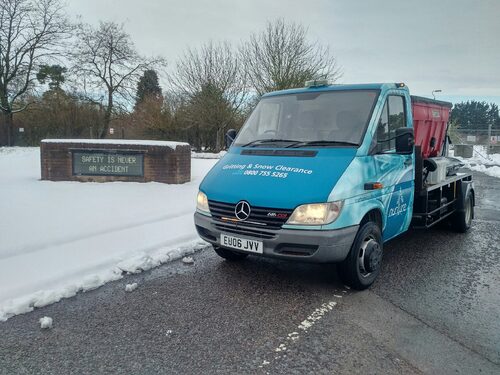 Gritter  parked at a site entrance on snowy road.